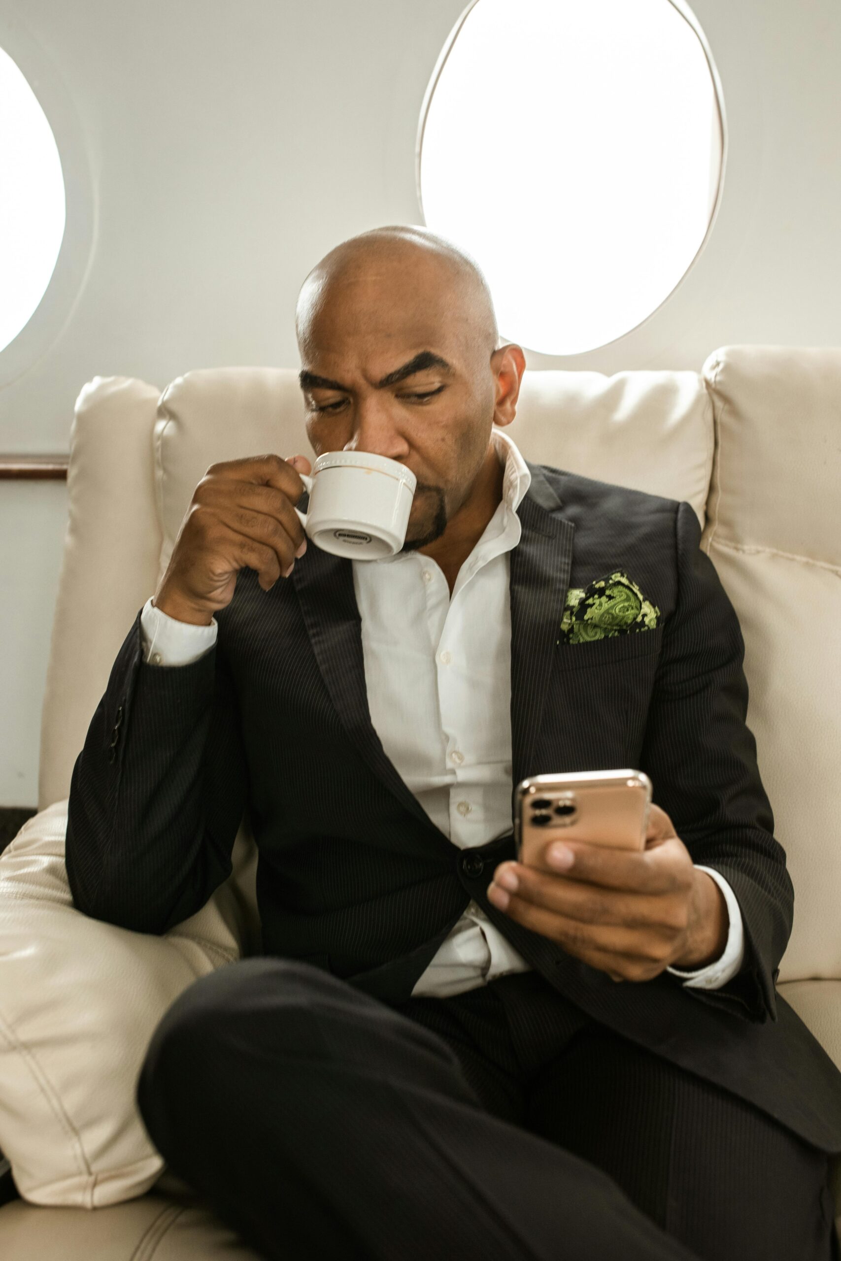 Elegantly dressed man enjoying a coffee while using his phone inside a private jet.